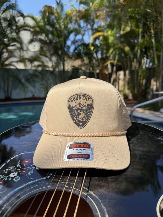Country Roads tan rope trucker hat with a laser-engraved leather patch, styled on an acoustic guitar