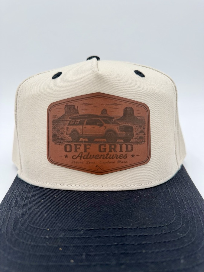 Off Grid Adventures cream and navy snapback with a large laser-engraved leather patch showing a truck in Monument Valley