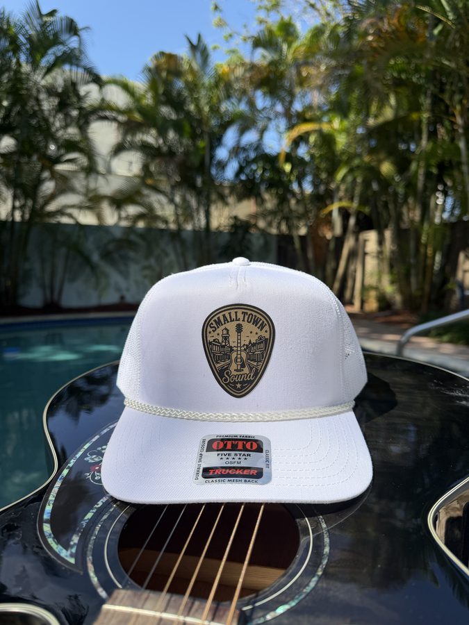 Small Town Sound white rope trucker hat with a laser-engraved leather guitar patch, on an acoustic guitar