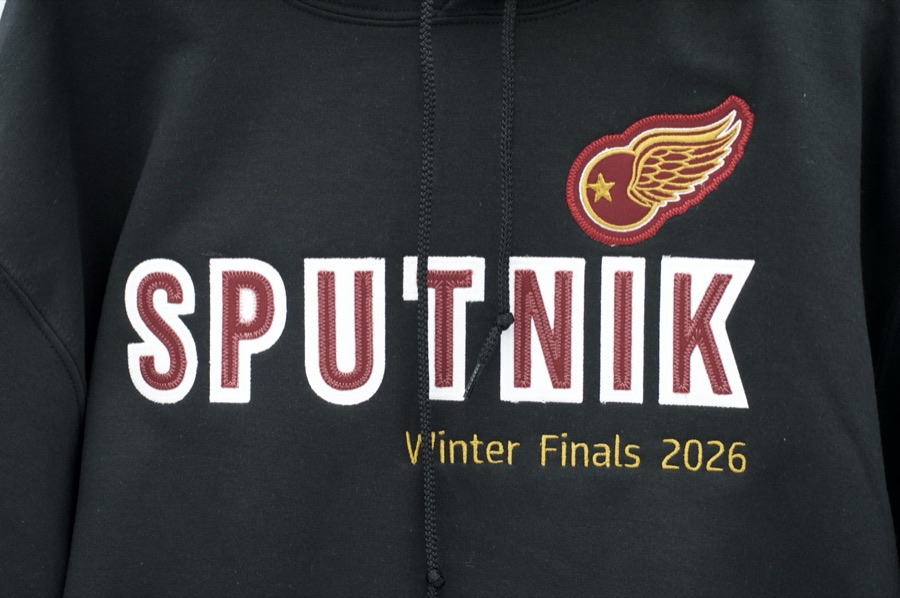 SPUTNIK Winter Finals 2026 hoodie chest detail — maroon tackle-twill letters with white satin-stitch outline and winged-wheel patch