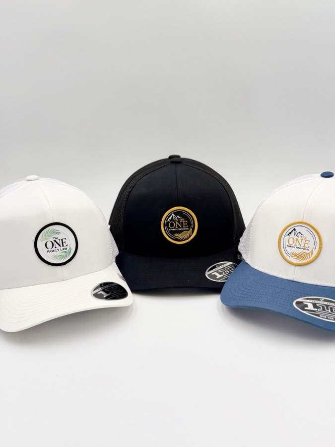The One branded trucker hats in white, black, and blue colorways with embroidered circular mountain patches